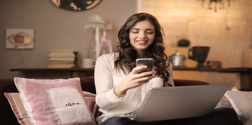 woman checking phone with laptop in front of her