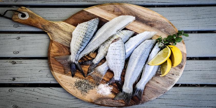 Unsplash. A bunch of fish on a circular wood board with pepper, salt, and lemon garnish