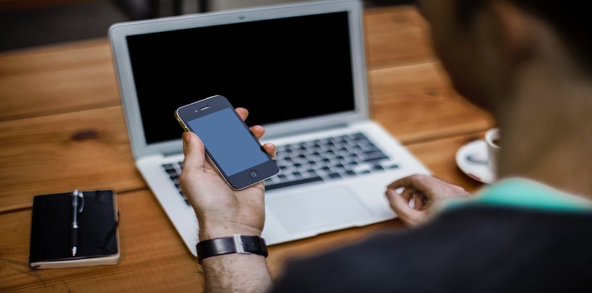 man working on laptop and using iphone