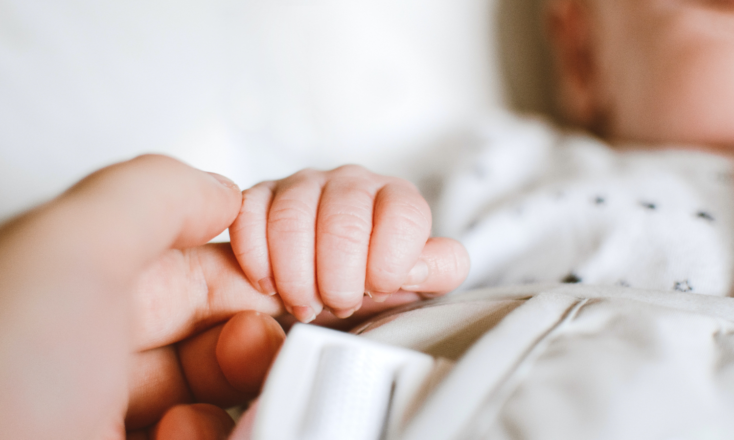 A baby hand holding an adult's hand